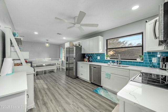 kitchen with decorative backsplash, sink, white cabinetry, stainless steel appliances, and light stone counters