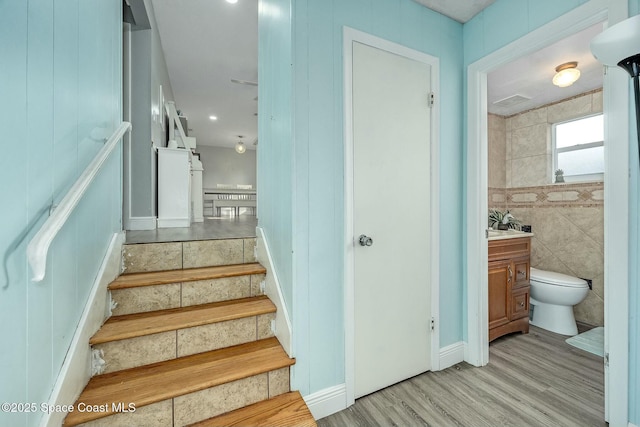 stairway with tile walls and hardwood / wood-style flooring