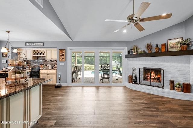 living room featuring dark hardwood / wood-style floors, a fireplace, ceiling fan with notable chandelier, and vaulted ceiling