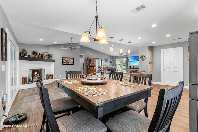 dining area with ceiling fan, light hardwood / wood-style floors, lofted ceiling, and a brick fireplace