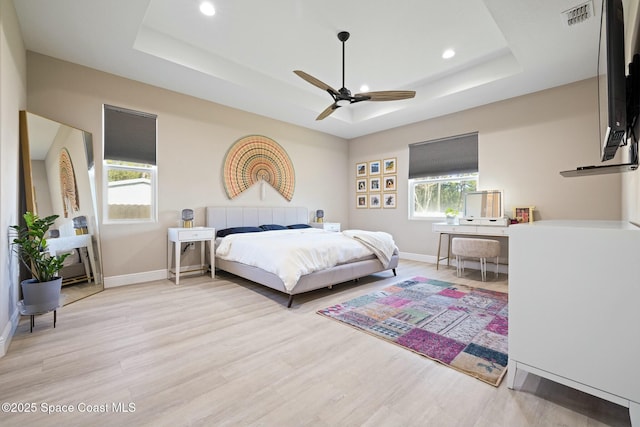 bedroom featuring light hardwood / wood-style flooring, a raised ceiling, and ceiling fan