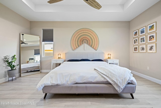 bedroom featuring light wood-type flooring, a tray ceiling, and ceiling fan