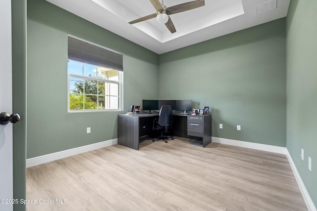 home office featuring ceiling fan, light wood-type flooring, and a tray ceiling