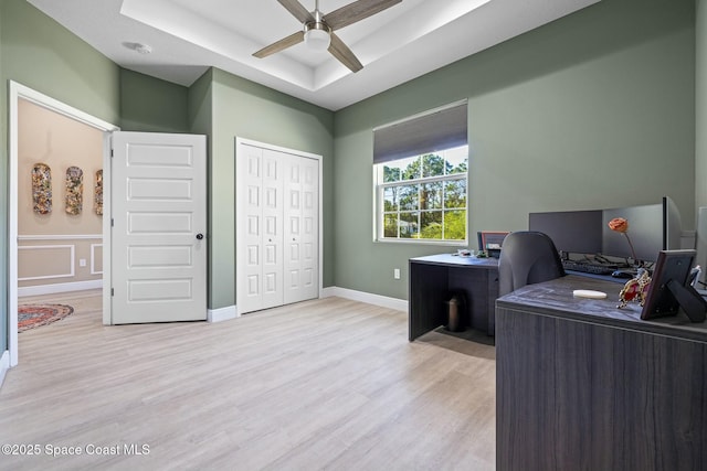 office space featuring ceiling fan, light wood-type flooring, and a tray ceiling