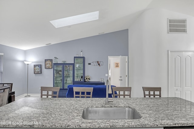 kitchen with light stone counters, sink, a kitchen island with sink, and vaulted ceiling with skylight