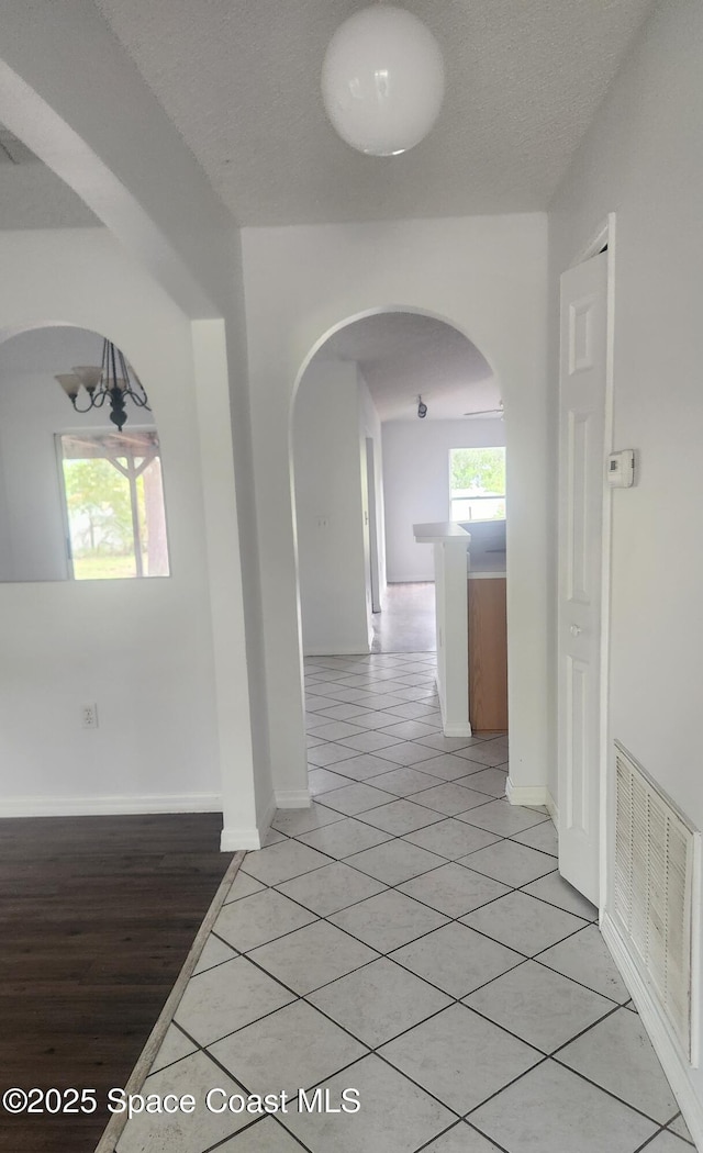 corridor featuring light tile patterned floors, a textured ceiling, and a chandelier