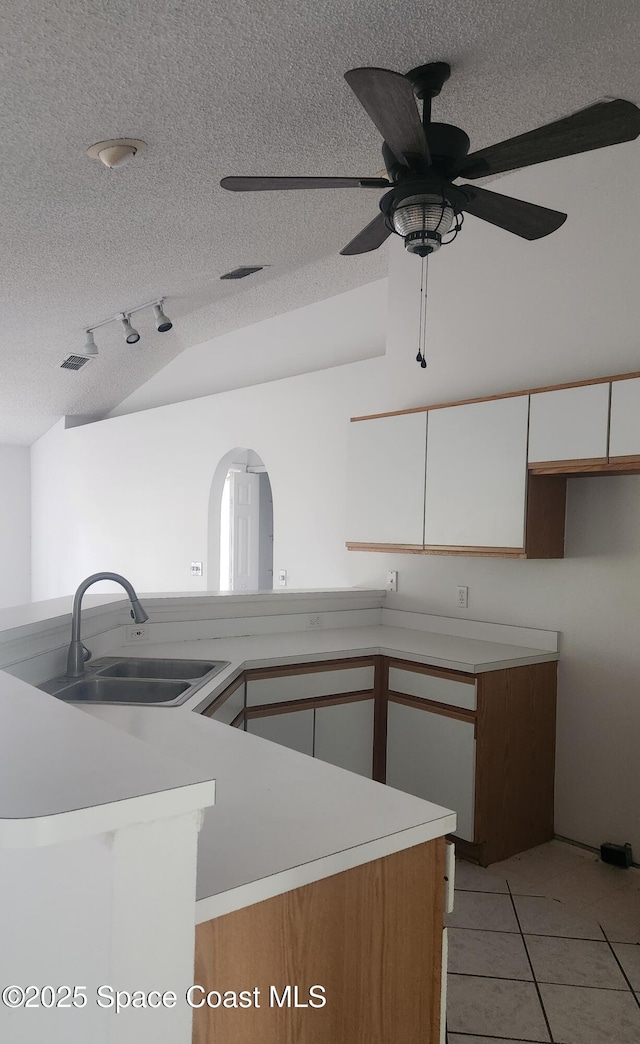 kitchen featuring vaulted ceiling, ceiling fan, sink, light tile patterned floors, and white cabinetry