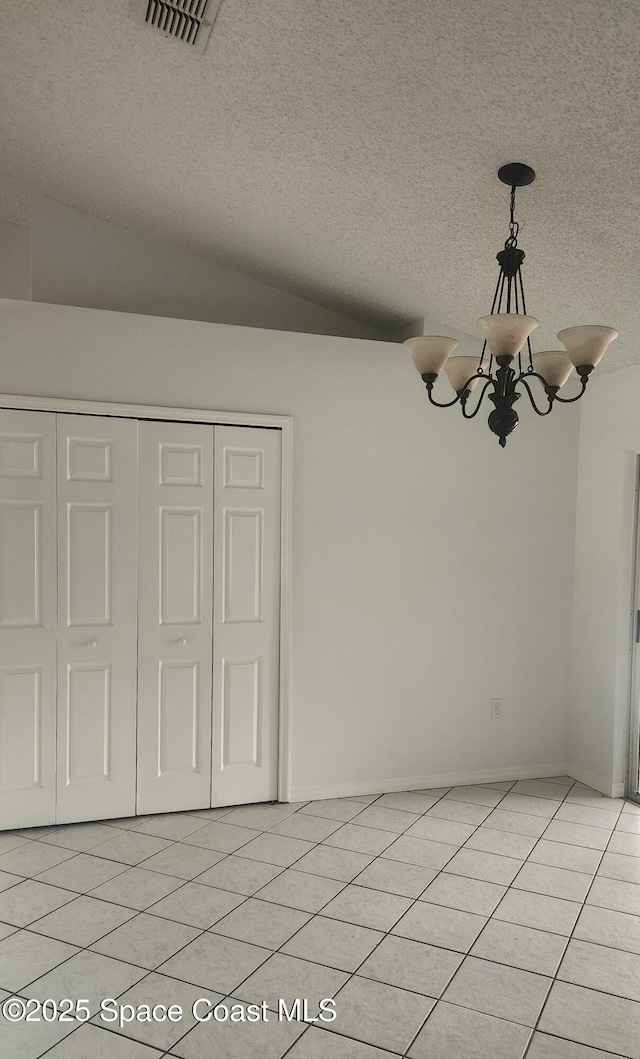 unfurnished dining area with a chandelier, light tile patterned floors, a textured ceiling, and vaulted ceiling