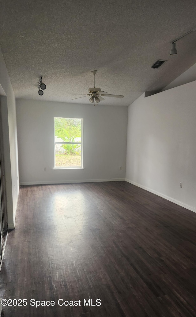 spare room featuring a textured ceiling, track lighting, ceiling fan, and dark wood-type flooring