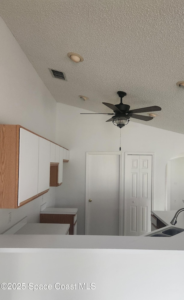 kitchen with white cabinetry, sink, ceiling fan, vaulted ceiling, and a textured ceiling