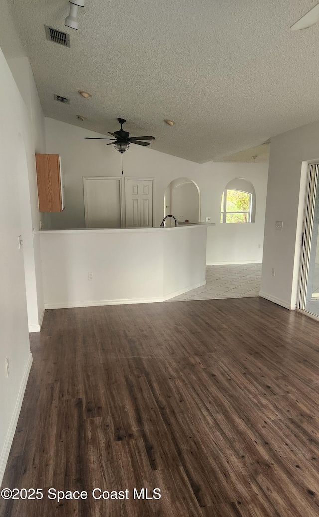 interior space with dark hardwood / wood-style flooring, a textured ceiling, vaulted ceiling, and ceiling fan