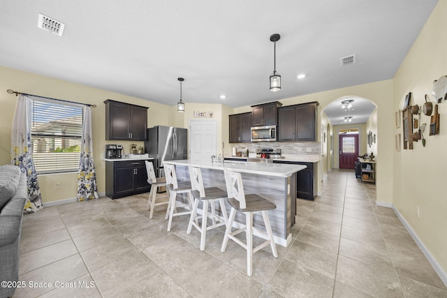 kitchen with pendant lighting, a center island with sink, appliances with stainless steel finishes, dark brown cabinets, and a breakfast bar area