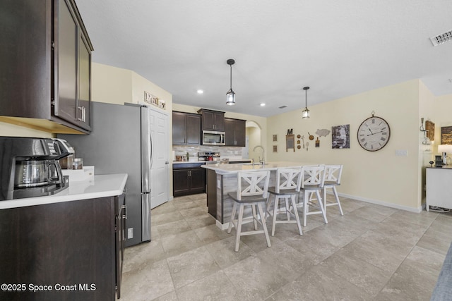 kitchen featuring a kitchen bar, dark brown cabinetry, a kitchen island with sink, sink, and pendant lighting