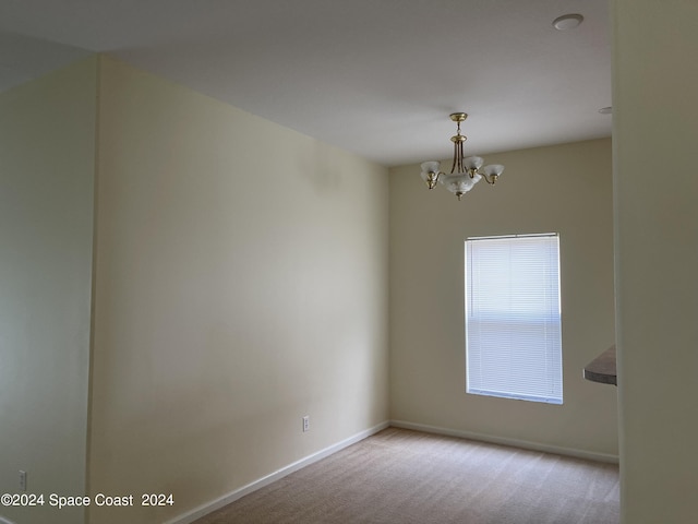 empty room featuring light colored carpet and a notable chandelier