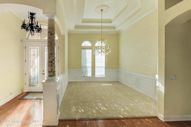 interior space with decorative columns, a tray ceiling, crown molding, hardwood / wood-style flooring, and a chandelier