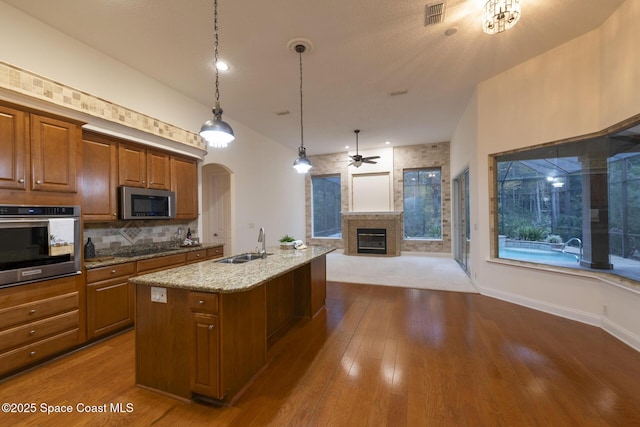 kitchen featuring sink, hanging light fixtures, stainless steel appliances, light stone counters, and a center island with sink