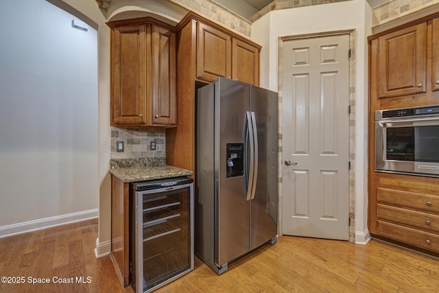 kitchen featuring beverage cooler, light stone counters, backsplash, appliances with stainless steel finishes, and light wood-type flooring