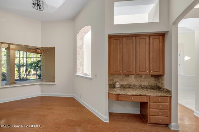 kitchen featuring light wood-type flooring, backsplash, light stone counters, built in desk, and a high ceiling