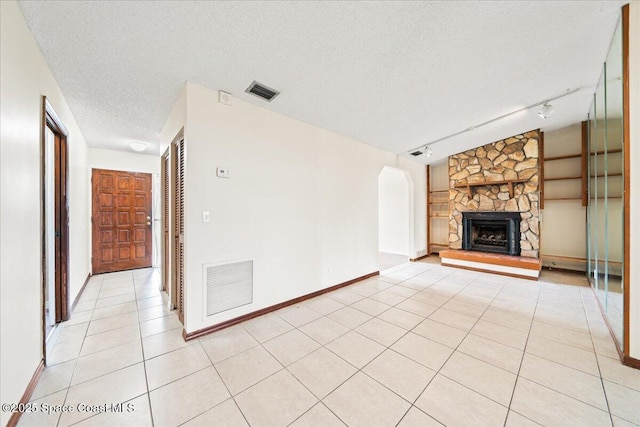 unfurnished living room with a textured ceiling, rail lighting, a stone fireplace, and light tile patterned flooring