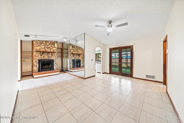 unfurnished living room with a stone fireplace, vaulted ceiling, ceiling fan, light tile patterned floors, and a textured ceiling