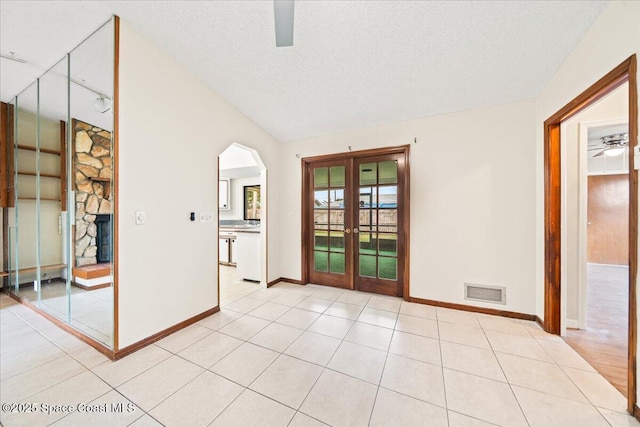 unfurnished room with lofted ceiling, french doors, ceiling fan, light tile patterned floors, and a textured ceiling