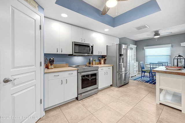 kitchen featuring stainless steel appliances, white cabinetry, ceiling fan, and a tray ceiling