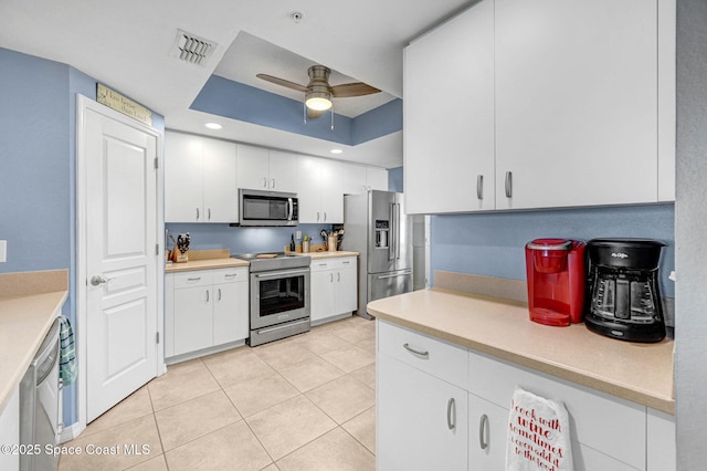 kitchen featuring ceiling fan, stainless steel appliances, white cabinets, light tile patterned flooring, and a raised ceiling