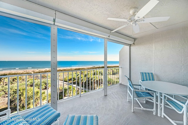 sunroom with a ceiling fan, a water view, and a beach view