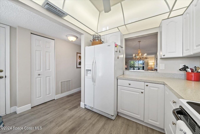 kitchen with stove, a textured ceiling, white refrigerator with ice dispenser, white cabinets, and a chandelier