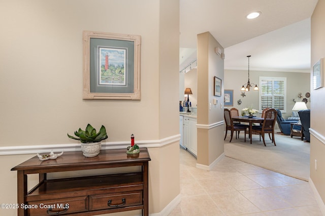 hall featuring a notable chandelier, light tile patterned flooring, and crown molding