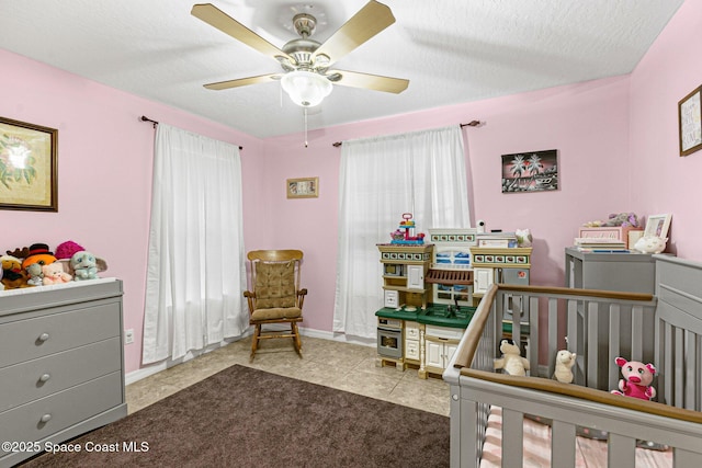 bedroom featuring ceiling fan, a textured ceiling, a crib, and light tile patterned floors