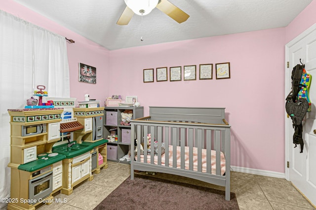 bedroom with light tile patterned floors, a textured ceiling, a nursery area, and ceiling fan