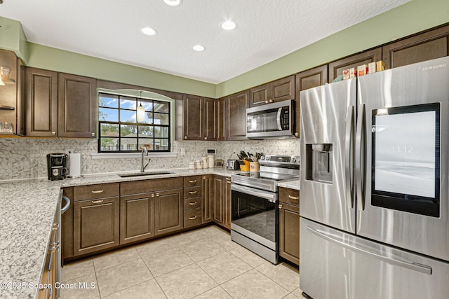 kitchen featuring stainless steel appliances, sink, light tile patterned floors, and dark brown cabinetry