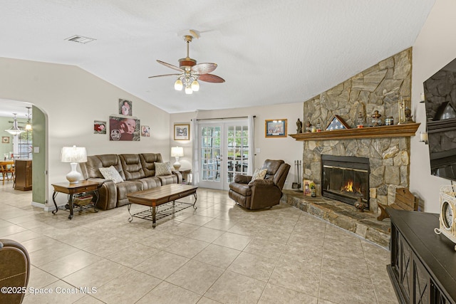 living room featuring a stone fireplace, lofted ceiling, light tile patterned floors, ceiling fan, and french doors