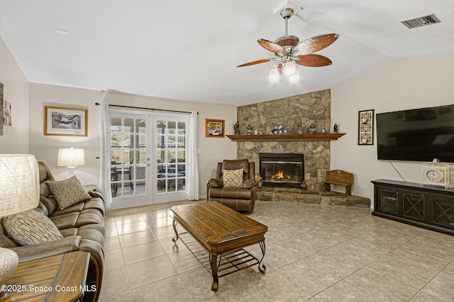 tiled living room featuring french doors, ceiling fan, a stone fireplace, and vaulted ceiling