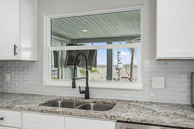 kitchen featuring light stone countertops, white cabinetry, stainless steel dishwasher, and sink