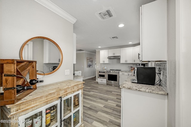 kitchen featuring light wood-type flooring, light stone countertops, stainless steel range oven, crown molding, and white cabinets