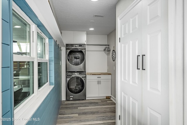 washroom with cabinets, a textured ceiling, dark hardwood / wood-style floors, and stacked washer and dryer