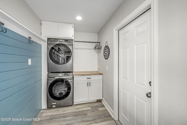 laundry area featuring cabinets, light hardwood / wood-style flooring, stacked washer and dryer, and wooden walls