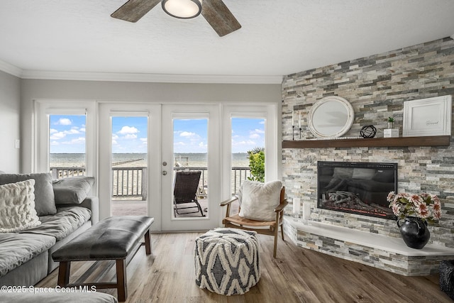 living room with crown molding, wood-type flooring, a wealth of natural light, and a stone fireplace