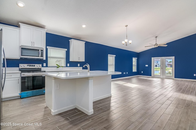 kitchen with light hardwood / wood-style flooring, appliances with stainless steel finishes, white cabinetry, hanging light fixtures, and an island with sink