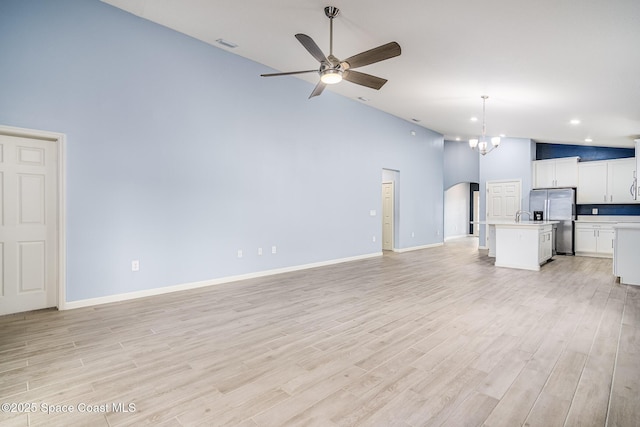 unfurnished living room featuring high vaulted ceiling, ceiling fan with notable chandelier, and light hardwood / wood-style floors