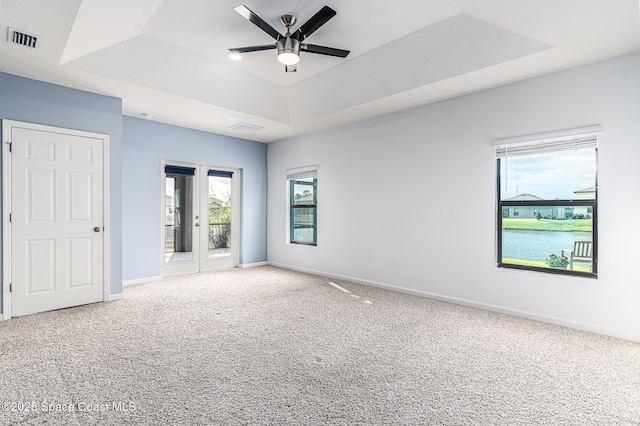 spare room with ceiling fan, a water view, carpet, a tray ceiling, and french doors