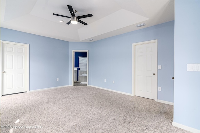 unfurnished bedroom with ceiling fan, ensuite bathroom, a raised ceiling, and carpet