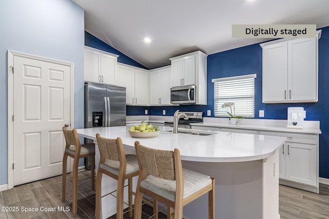 kitchen with a breakfast bar, sink, appliances with stainless steel finishes, a kitchen island with sink, and white cabinets