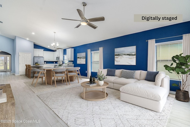 living room with high vaulted ceiling, ceiling fan with notable chandelier, and light hardwood / wood-style flooring