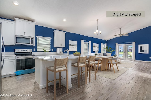 kitchen with a breakfast bar area, pendant lighting, stainless steel appliances, a kitchen island with sink, and white cabinets