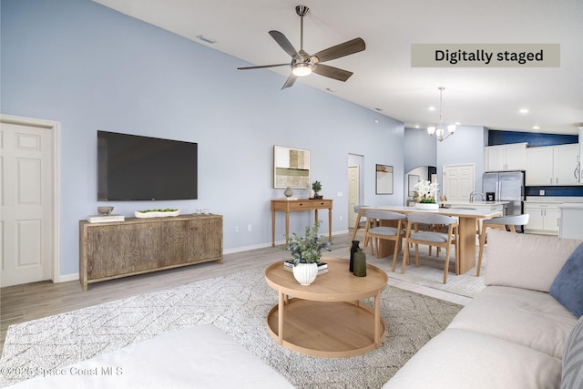 living room featuring ceiling fan with notable chandelier, high vaulted ceiling, and light wood-type flooring