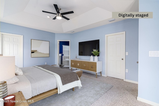 bedroom with a raised ceiling, ensuite bathroom, carpet, and ceiling fan