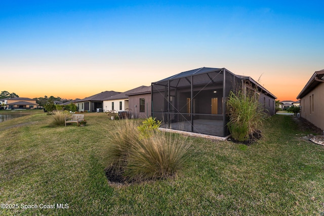 back house at dusk featuring a patio area, a lawn, and glass enclosure